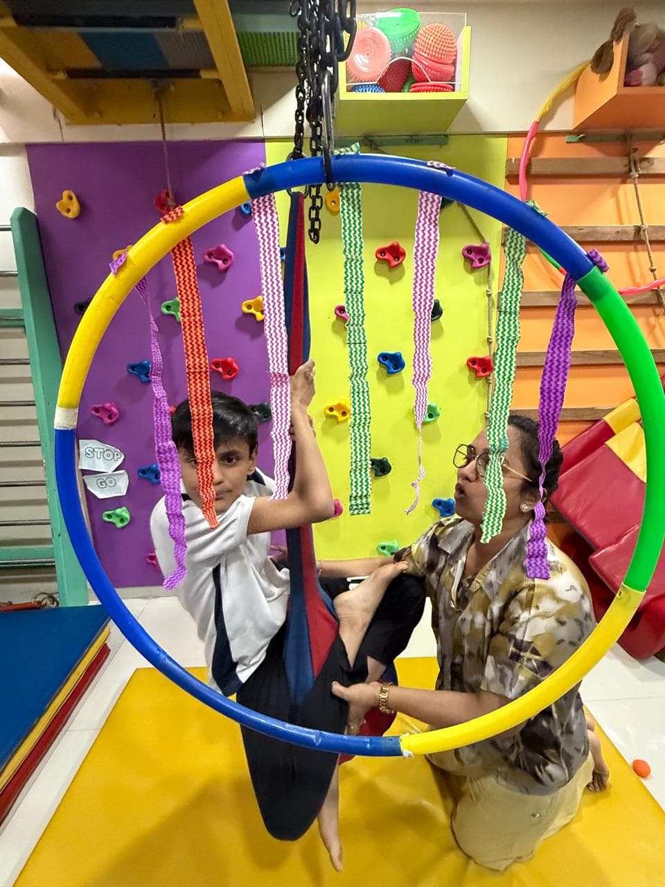 A boy on a hoop swing in the sensory gym with therapist support