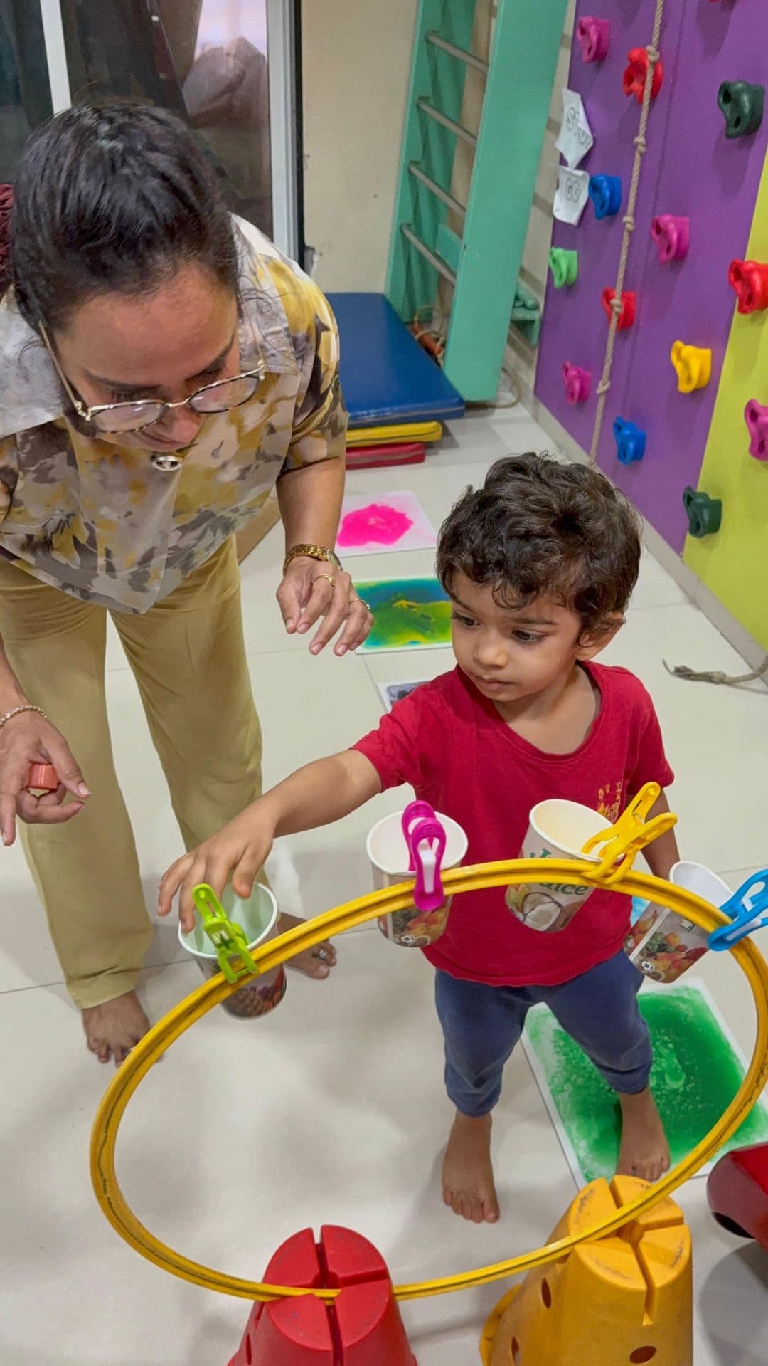 Therapist guiding a child through a playful balance and coordination activity with clinic equipment