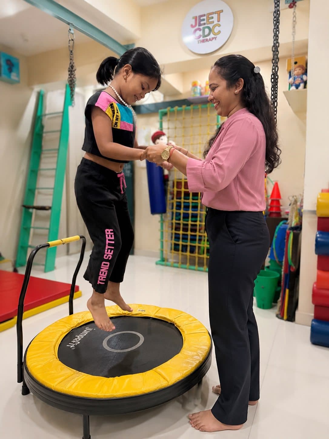 Girl jumping on a mini trampoline with hand support from a smiling therapist