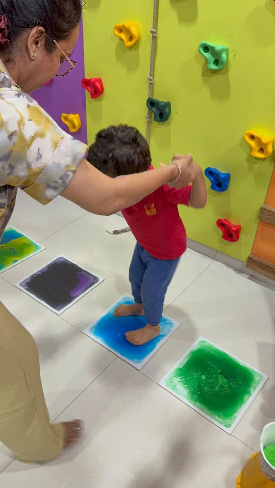 Child using colorful tactile stepping pads with therapist support in a sensory therapy room