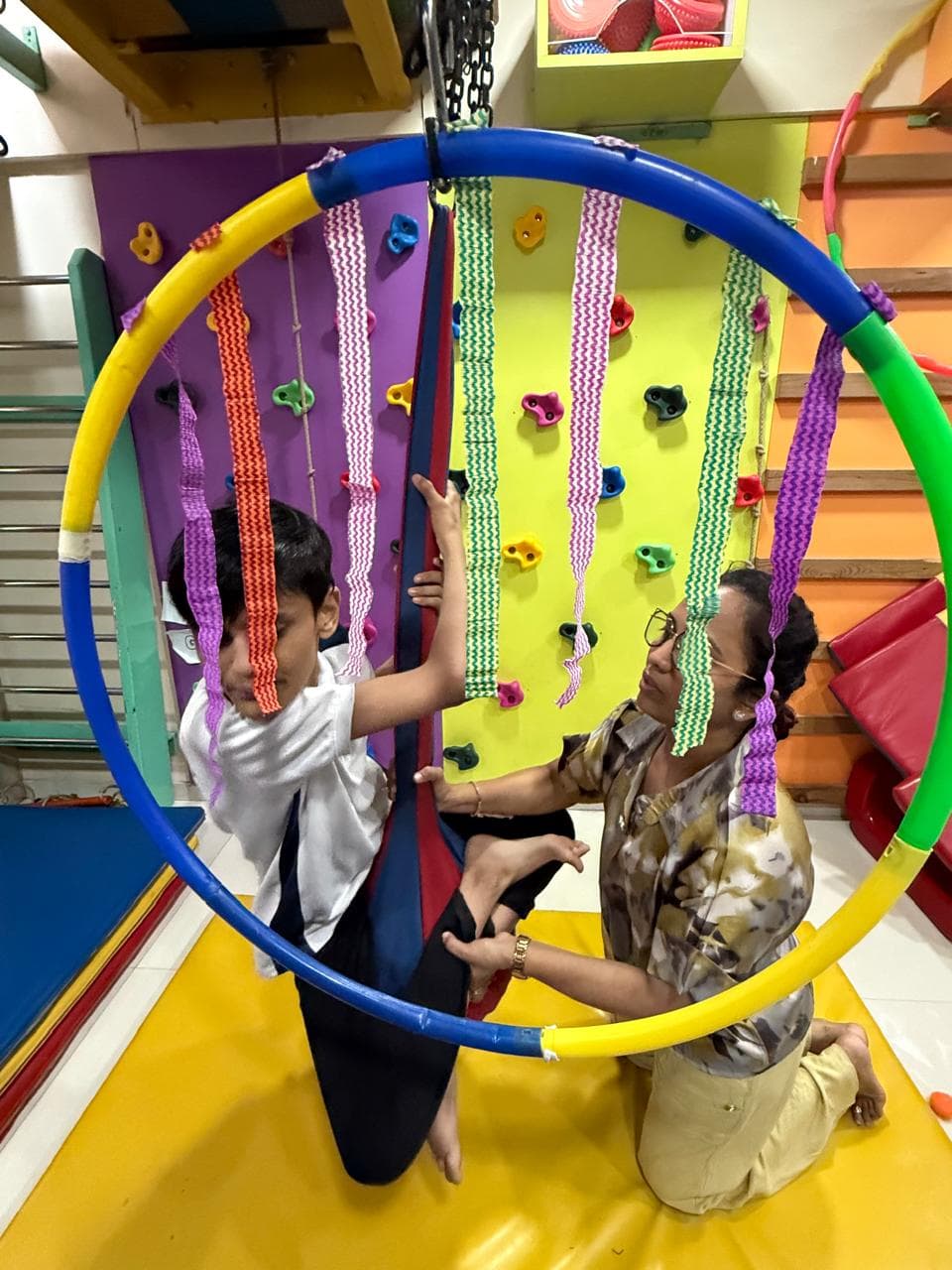 Dr. Sharuja supporting a child on hoop swing equipment in the sensory gym